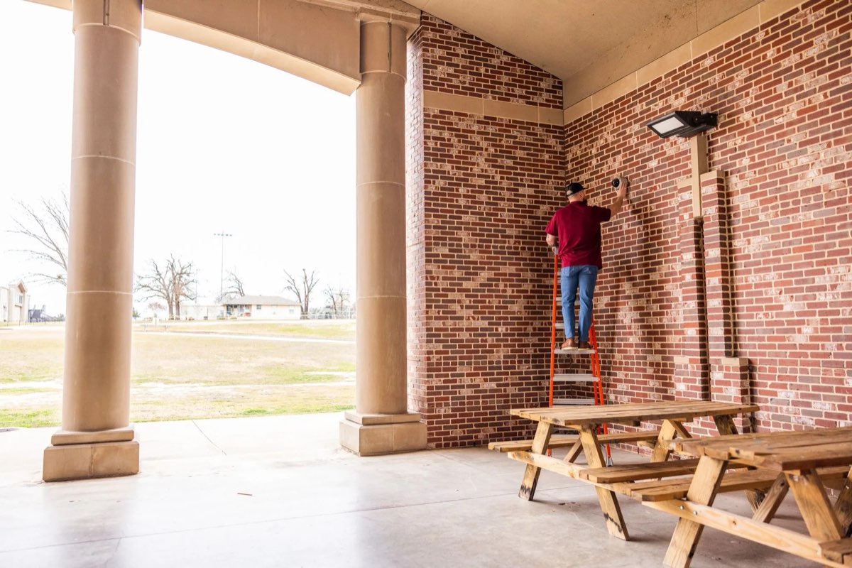 Alarm Masters technician on a ladder installing a dome security camera on the brick exterior of a Texas commercial building