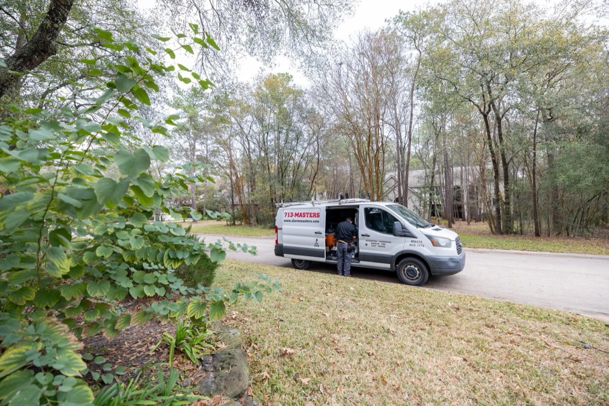 Alarm Masters technician unloading equipment from a branded service van at a Texas job site